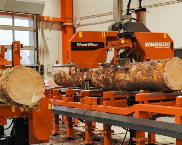 Pomarańczowa maszyna do obróbki drewna Wood-Mizer WM2500 przetwarza pień drzewa na deski.