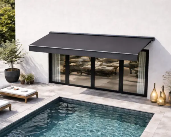 Un store banne gris protège une terrasse moderne avec piscine. L'entretien de ce store est essentiel pour profiter de cet espace de détente.