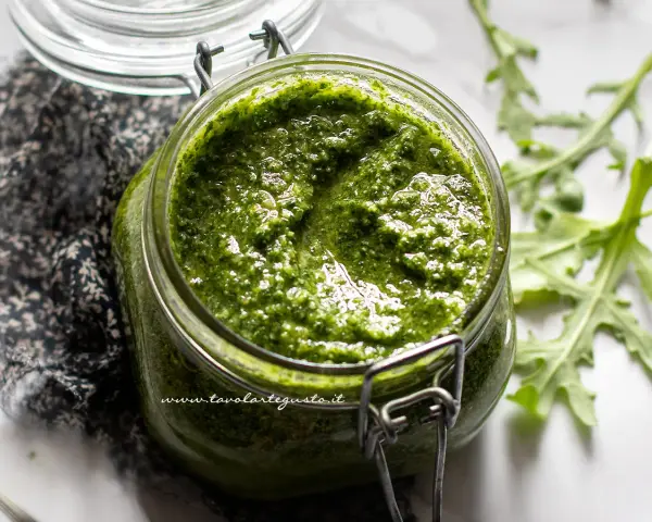 Un vasetto di pesto di rucola fatto in casa, con foglie di rucola fresca sullo sfondo.