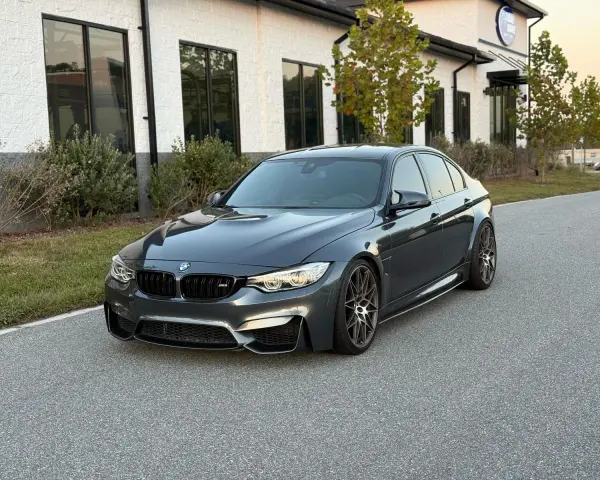 Szary sedan BMW M3 na tle nowoczesnego budynku. Sprawdź aktualną bmw m3 cena i możliwości tego sportowego auta.