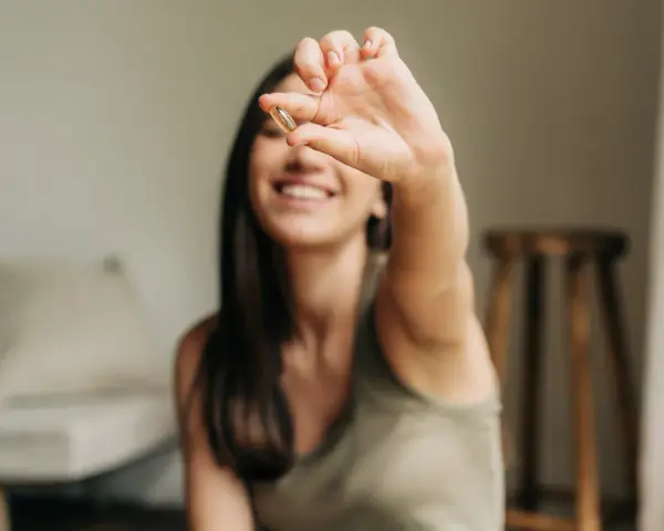 Une jeune femme souriante tient une capsule, symbole d'une cure de vitamine pour un bien-être quotidien.