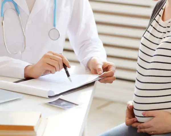 Lekarz omawia z ciężarną pacjentką kolejne trymestry ciąży, notując coś na dokumentach.