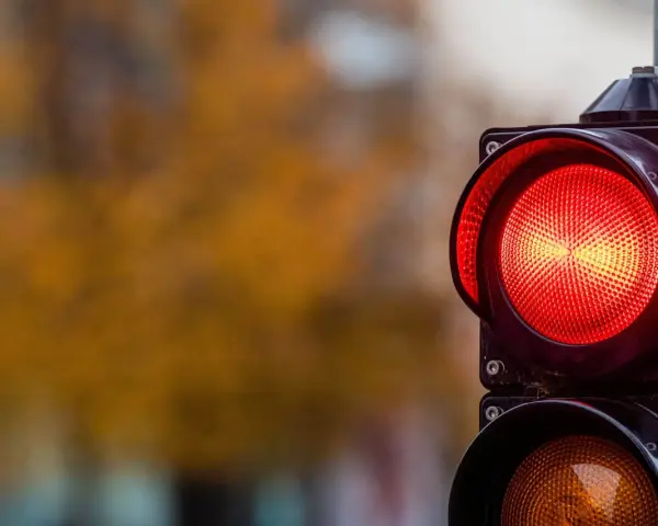 Close-up of a red traffic light with a blurred background of autumn foliage.