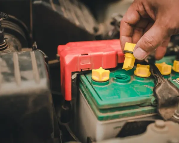 A hand removes a yellow cap from a truck battery, hinting at maintenance to ensure it lasts as long as possible.