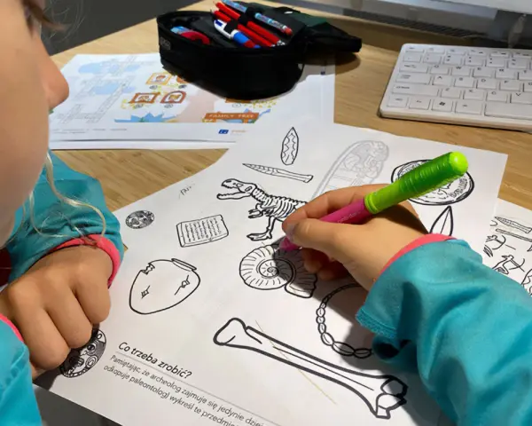 Dziecko koloruje edukacyjne karty pracy z dinozaurem i artefaktami.