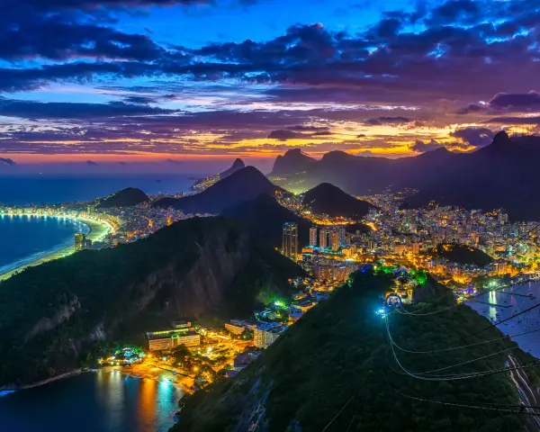 Zachód słońca nad słynną plażą w Rio de Janeiro. Miasto rozświetlone tysiącami świateł, góry i ocean tworzą magiczny widok.