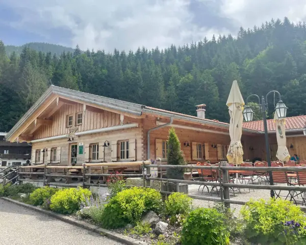 Holzhütte mit Biergarten und blühenden Blumen vor einer Bergkulisse. Die untere Firstalm lädt zum Verweilen ein.