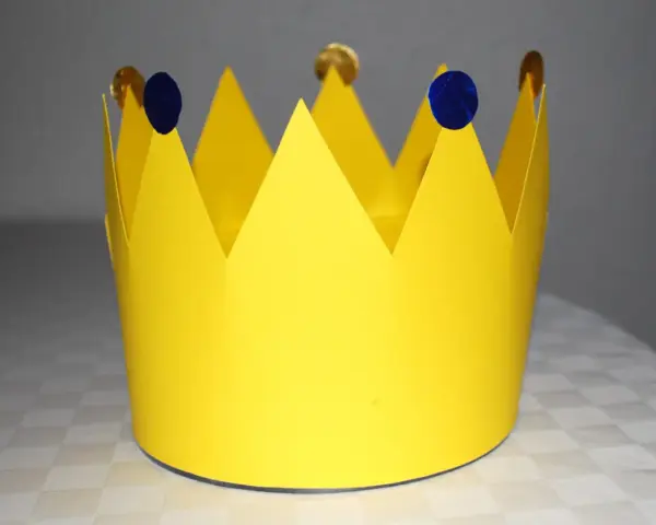 Gelbe Papierkrone, die zum **krone basteln** einlädt. Mit blauen Tupfern und goldenen Münzen verziert, wartet sie auf ihren kleinen König oder ihre kleine Königin.