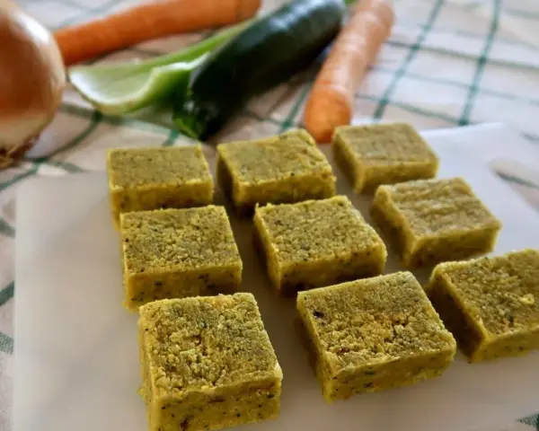Cubetti di dado vegetale fatto in casa, pronti per insaporire le tue ricette. Sullo sfondo, ingredienti freschi come carote, zucchine e cipolla.