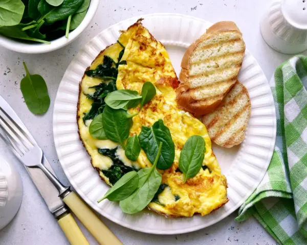Pyszny omlet ze szpinakiem, podany z grzankami i świeżymi liśćmi szpinaku. Idealne śniadanie pełne witamin.
