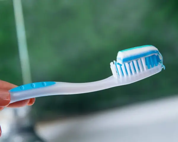 Dłoń trzymająca szczoteczkę z biało-niebieską pastą. Idealna jaka pasta po wybielaniu zębów dla lśniącego uśmiechu.