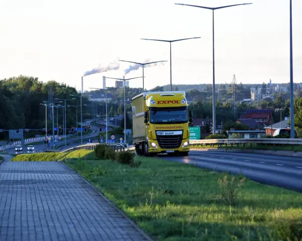 Żółta ciężarówka EXPOL jedzie drogą, symbolizując mobilność i wyzwania związane z pakietem mobilności a umową zlecenie.