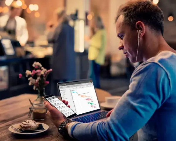 Hombre revisa datos de business intelligence hostelería en su laptop y móvil, sentado en una cafetería.