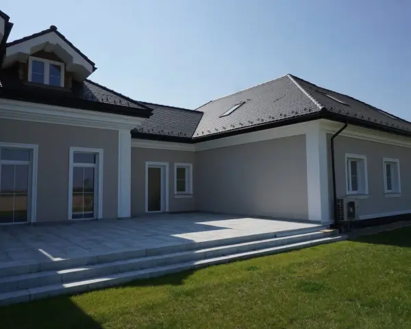 Nowoczesny dom z tarasem i trawnikiem. Elegancki gzyms podkreśla architekturę budynku.