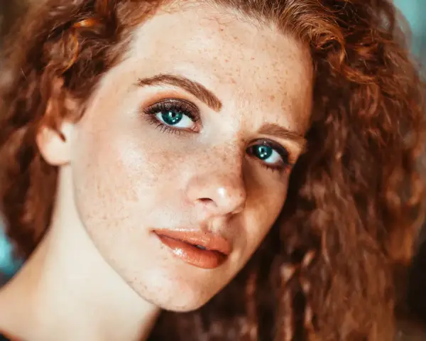 Primo piano di una ragazza con lentiggini e capelli rossi, con un trucco naturale che esalta la sua bellezza.