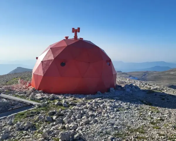 Il rifugio Manzini, una cupola rossa geodetica, si erge su un crinale roccioso sotto un cielo azzurro.