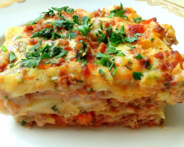 Pyszna lasagne Ani Starmach, z warstwami mięsa, sosu i sera, posypana świeżą natką pietruszki.