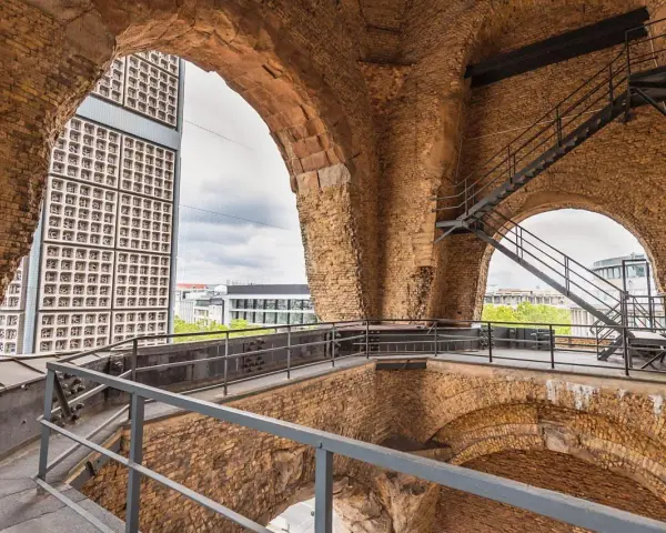 Blick durch die Bögen der Kaiser-Wilhelm-Gedächtniskirche auf eine moderne Glasfassade und Treppen.