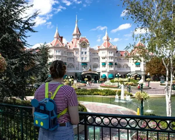Dziewczyna z plecakiem w kształcie Myszki Miki podziwia zamek w Disneyland Paris. Bilety do parku już kupione, czas na przygodę!