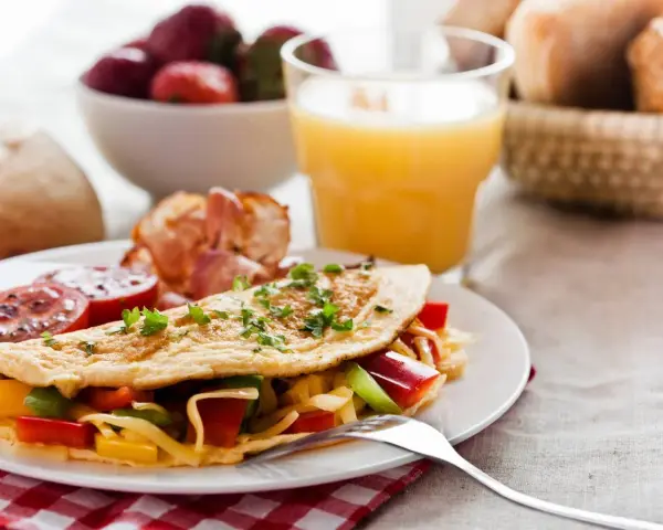 Pyszne śniadanie bez chleba: omlet z warzywami i serem, bekon, pomidory, truskawki i sok pomarańczowy.