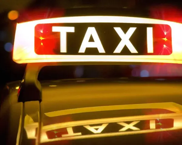 Leuchtendes TAXI-Schild mit roten Blinklichtern, das einen Taxi-Alarm signalisiert. Die Reflexion auf dem dunklen Auto verstärkt die nächtliche Atmosphäre.