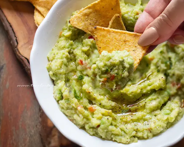 Un chip di mais raccoglie il cremoso guacamole, mostrando come fare il guacamole fresco e delizioso.