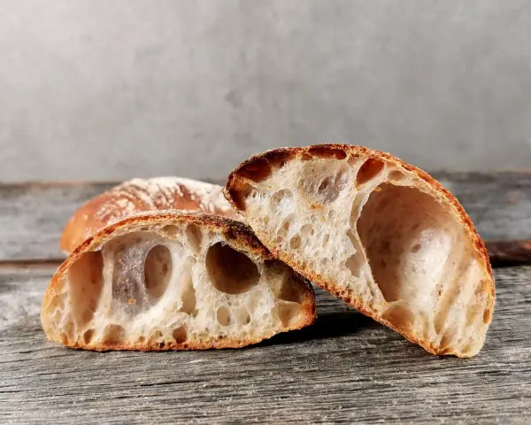 Zwei Hälften eines rustikalen ciabatta mit sauerteig, mit großer, luftiger Krume und knuspriger Kruste, liegen auf einem Holzbrett.
