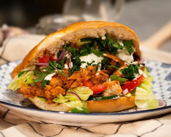 Pyszny, domowy kebab z kurczaka z piekarnika, pełen świeżych warzyw i sosu, na ozdobnym talerzu.