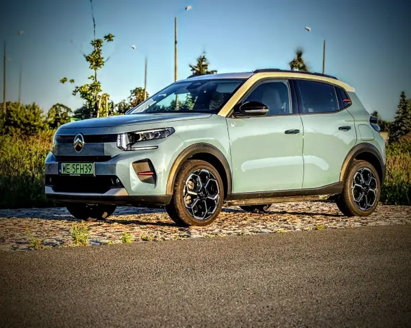 Jasnoszary Citroën ë-C3 z żółtym dachem stoi na tle drzew i nieba.
