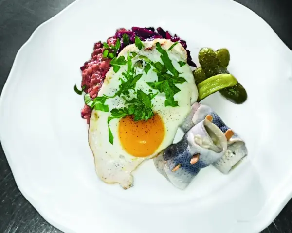 Labskaus mit Spiegelei, Rollmops und Gewürzgurken. Die Herkunft dieses norddeutschen Gerichts ist Seefahrer-Tradition.