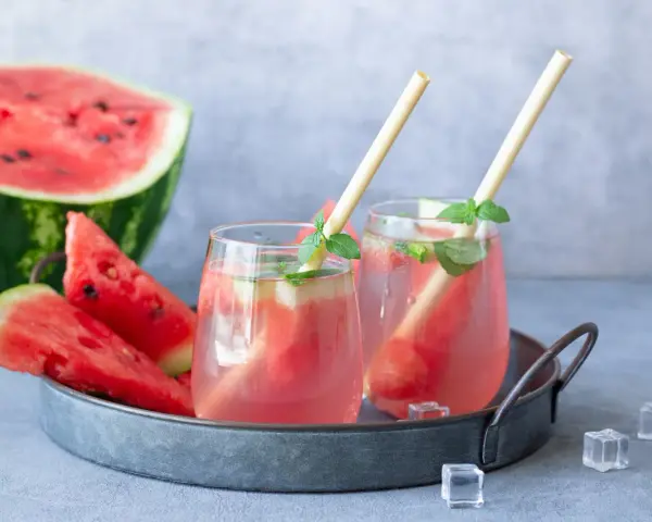 Orzeźwiający drink z arbuzem i miętą, podany na tacy z kawałkami arbuza i kostkami lodu. Idealny na upalne dni.