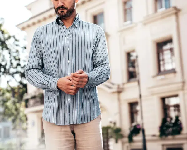 Mężczyzna w paski koszuli, z rękami złożonymi na brzuchu, idealnie pokazuje, kiedy koszula w spodnie tworzy elegancki look.