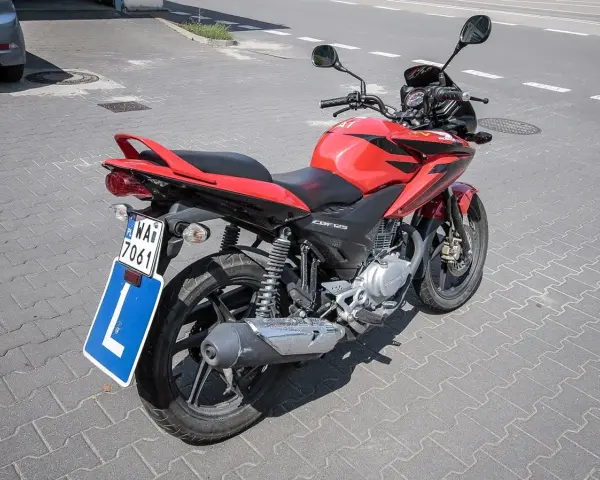 Czerwony motocykl Honda CBF125 z tablicą "L" i numerem rejestracyjnym WA7 7061, gotowy do nauki jazdy na prawo jazdy a1.
