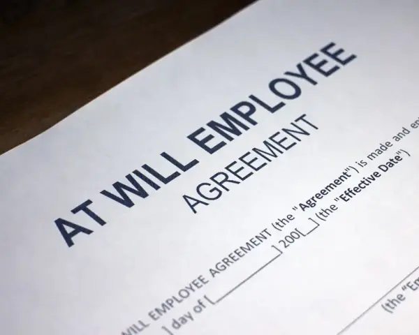 Close-up of an "At Will Employee Agreement" document, illustrating what does at-will employment mean: either party can terminate the relationship at any time.