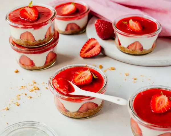 Mehrere kleine Gläser mit einem cremigen Dessert mit Erdbeeren und einer roten Erdbeersauce.