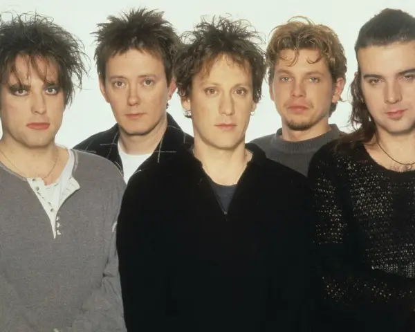 Pięciu członków zespołu The Cure pozuje do zdjęcia. Robert Smith z charakterystyczną fryzurą i makijażem na pierwszym planie.