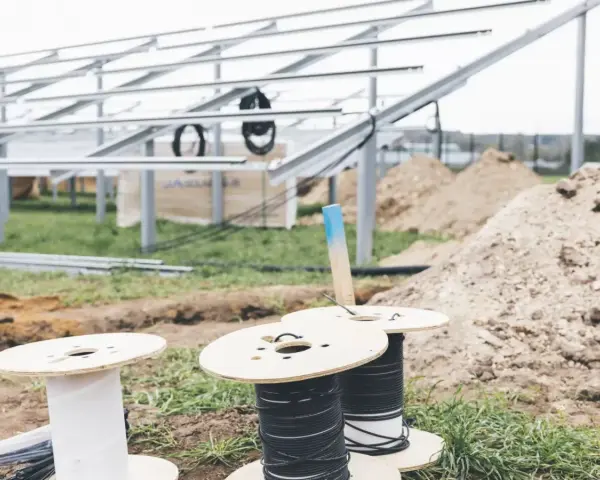 Na placu budowy paneli słonecznych przygotowywane są kable do uziemienia. Widać szpule z przewodami i metalowe konstrukcje.
