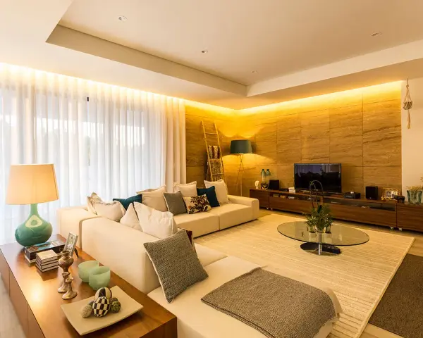 Salón moderno con sofá blanco, mesa de centro de cristal y **luz indirecta** que ilumina la pared de piedra y las cortinas.