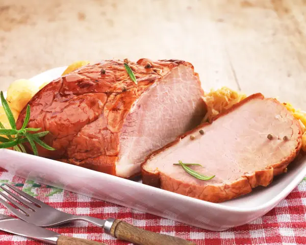 Pyszny, pieczony schab na wielkanoc, udekorowany rozmarynem i ziarnami pieprzu, podany z ziemniaczkami i surówką.
