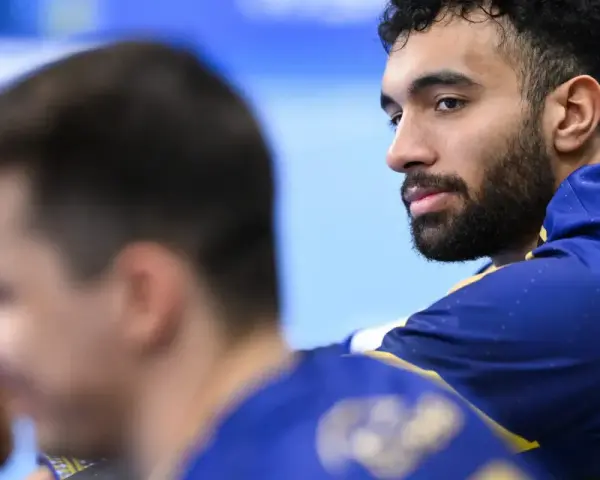 Hassan Kaddah, z brodą i kręconymi włosami, w niebieskiej bluzie z żółtymi detalami, spogląda w bok.