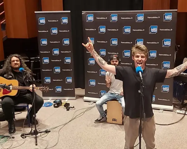 Un groupe rock alternatif français en pleine performance, avec un guitariste, un percussionniste et un chanteur énergique.