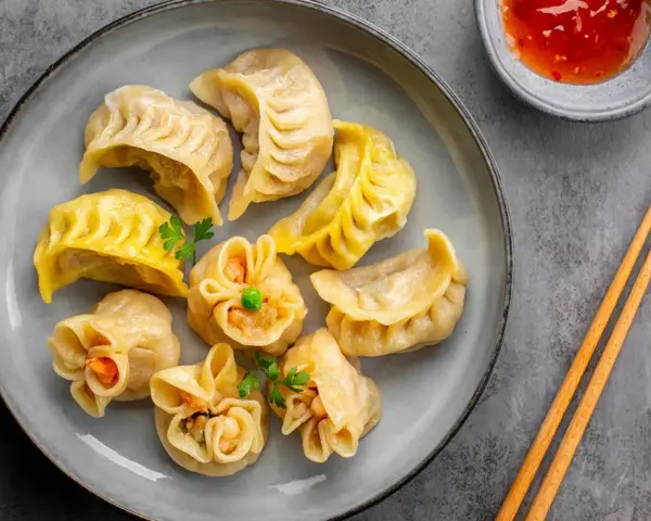 Talerz pełen aromatycznych chińskich pierożków, gotowych do zanurzenia w sosie. Obok pałeczki i miseczka z ostrym dipem.