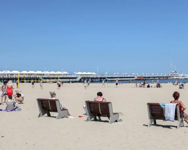Ludzie odpoczywają na plaży, ciesząc się słońcem i widokiem na molo. To idealne miejsce na polską riwierę.