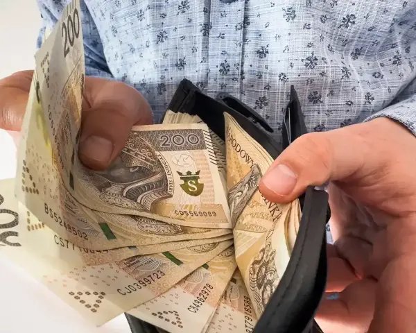 Ręce trzymają portfel z banknotami 200 zł. To symbol nagrody jubileuszowej za 40 lat pracy w budżetówce.