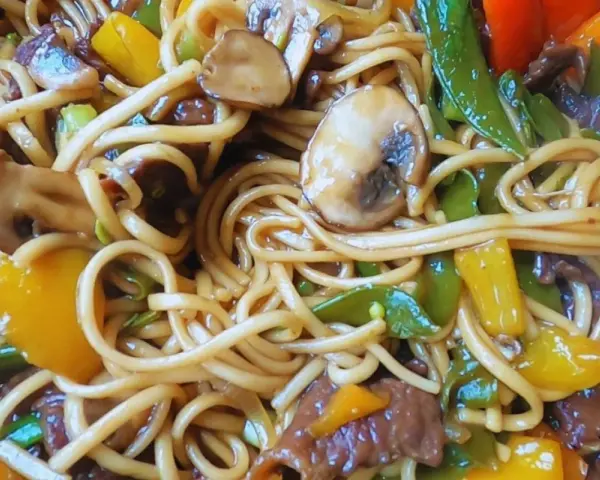 Udon z wołowiną przepis: sycące danie z grubym makaronem, kawałkami wołowiny, pieczarkami, papryką i zielonym groszkiem w sosie.