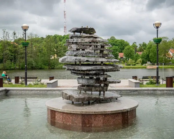 Kamienna rzeźba-fontanna nad jeziorem, jedna z atrakcji Czosu. W tle drzewa i budynki.