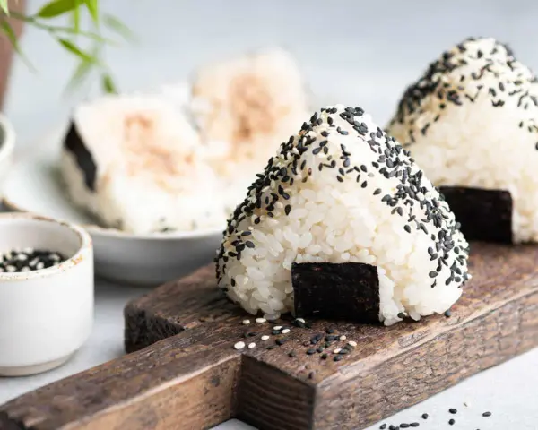 Trójkątne onigiri sushi z czarnym sezamem i kawałkiem nori na drewnianej desce.