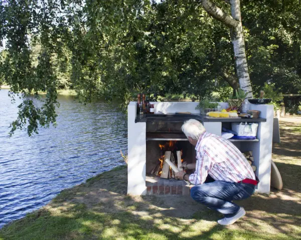 Man tänder en brasa i en nybyggd grill av tegelstenar vid en sjö.