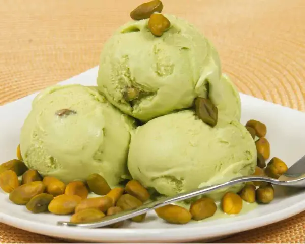 Tre palline di cremoso gelato al pistacchio, guarnite con pistacchi interi, su un piatto bianco con una spolverata di pistacchi tostati.