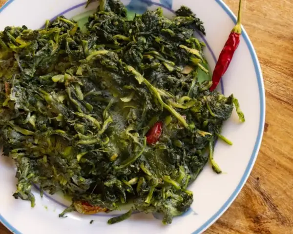 Un piatto di cicoria in padella, condita con peperoncino rosso e un filo d'olio d'oliva, su un tavolo di legno.